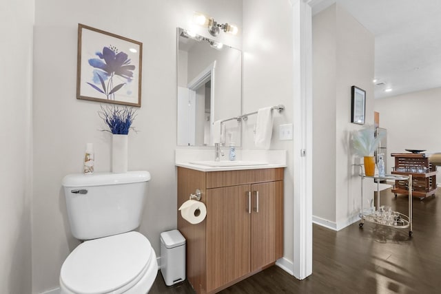 half bathroom featuring toilet, baseboards, wood finished floors, and vanity