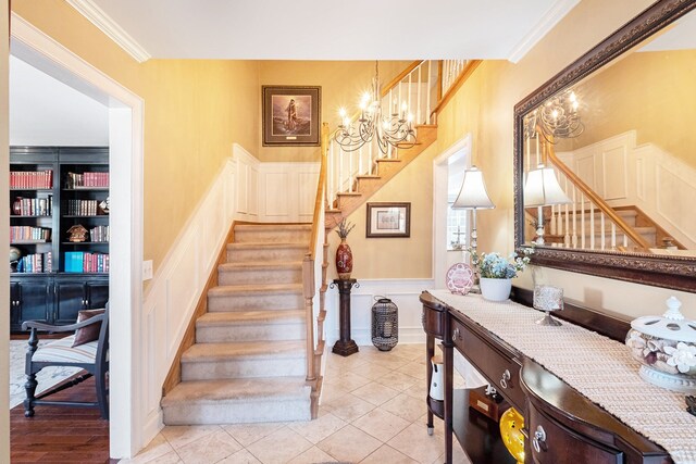 stairway featuring tile patterned flooring, wainscoting, an inviting chandelier, ornamental molding, and a decorative wall