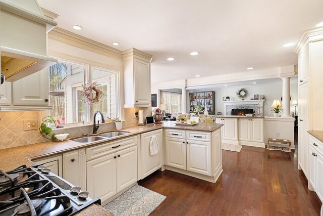 kitchen featuring a fireplace, a sink, a peninsula, dark wood-style floors, and open floor plan