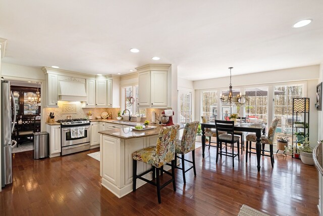 kitchen with a peninsula, custom exhaust hood, a sink, a notable chandelier, and stainless steel appliances