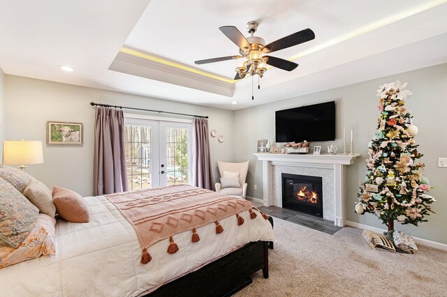 carpeted bedroom featuring a glass covered fireplace, access to exterior, baseboards, a raised ceiling, and french doors
