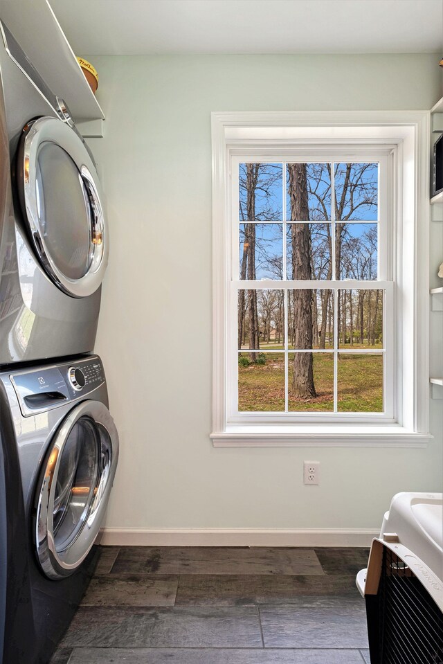 laundry room with baseboards, laundry area, stacked washer / drying machine, and dark wood-type flooring
