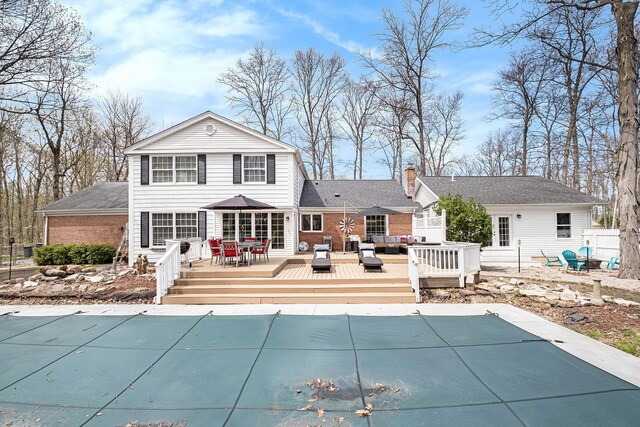 back of property with a covered pool, a wooden deck, outdoor lounge area, outdoor dining area, and a chimney