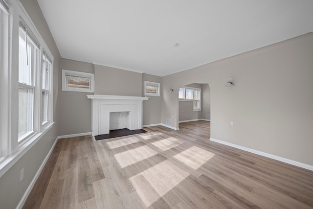 15866 Woodingham Dr, Detroit, MI 48238 - unfurnished living room featuring arched walkways, baseboards, a fireplace with flush hearth, and light wood finished floors