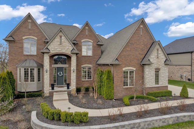 french country style house featuring brick siding, stone siding, and roof with shingles