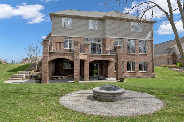 rear view of house with a lawn, brick siding, a fire pit, and a patio area