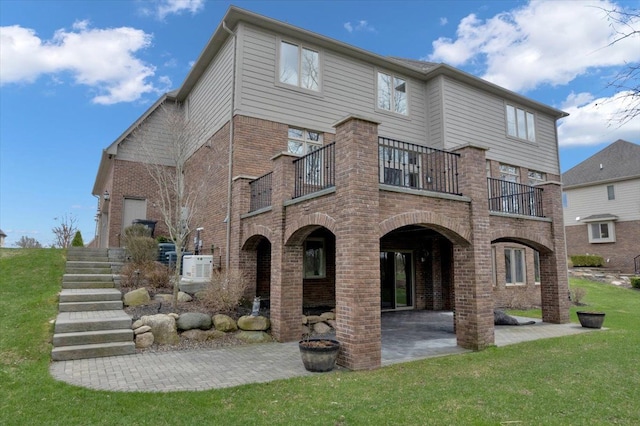rear view of house featuring a patio, a yard, brick siding, and a balcony