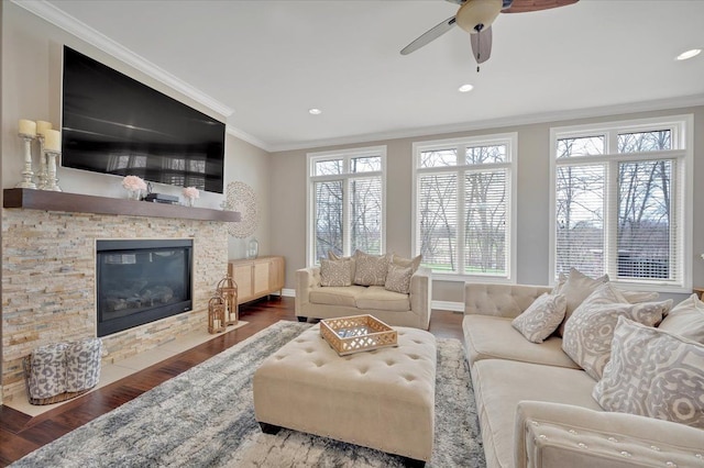 living area with crown molding, a ceiling fan, wood finished floors, and a stone fireplace