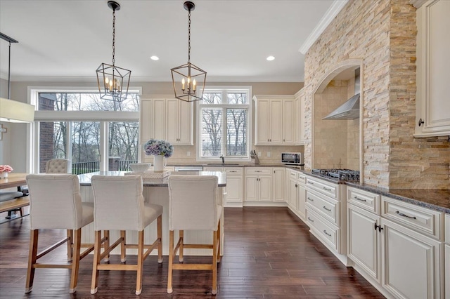 kitchen featuring crown molding, wall chimney range hood, hanging light fixtures, a breakfast bar area, and backsplash