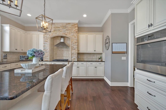 kitchen featuring wall chimney exhaust hood, a chandelier, dark wood finished floors, appliances with stainless steel finishes, and backsplash