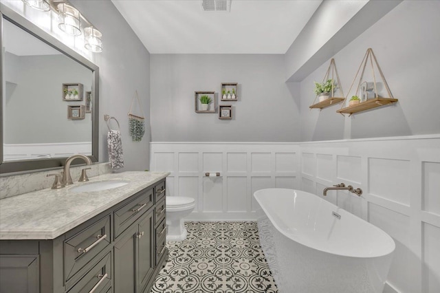 full bath with visible vents, vanity, a freestanding tub, a decorative wall, and a wainscoted wall