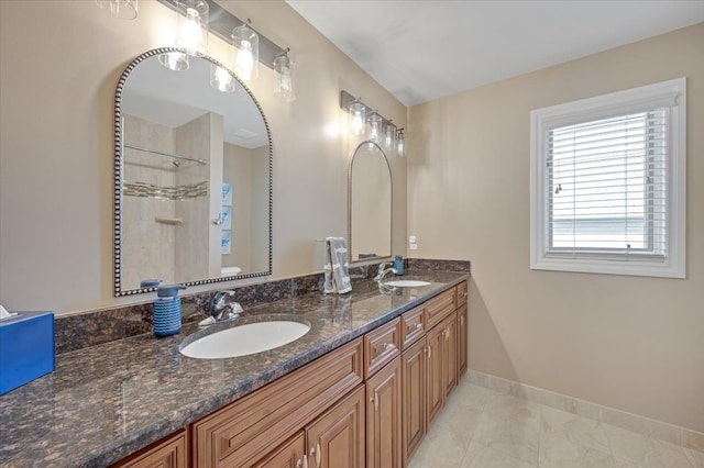 bathroom featuring a sink, tiled shower, baseboards, and double vanity