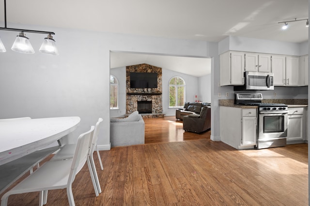 kitchen featuring a stone fireplace, appliances with stainless steel finishes, light wood finished floors, lofted ceiling, and white cabinetry
