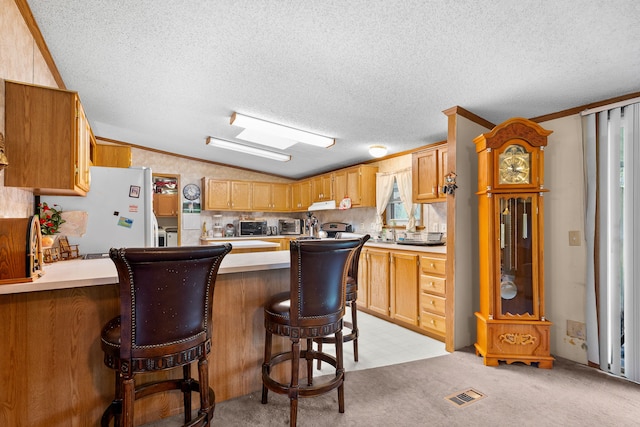 kitchen with a breakfast bar, light countertops, freestanding refrigerator, a peninsula, and visible vents