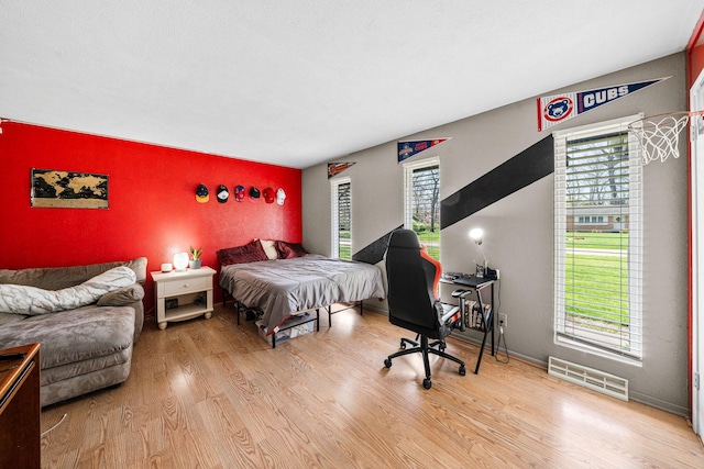 bedroom featuring visible vents, wood finished floors, and an accent wall