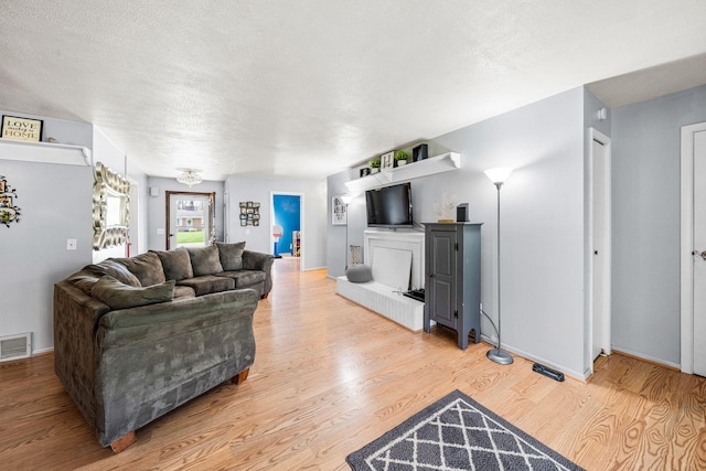 living room featuring baseboards, a textured ceiling, visible vents, and wood finished floors