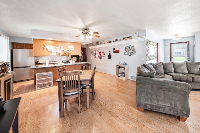 dining space featuring light wood-style floors, ceiling fan, a textured ceiling, and visible vents