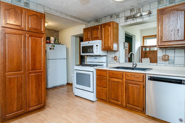 kitchen featuring a sink, brown cabinets, white appliances, and light countertops