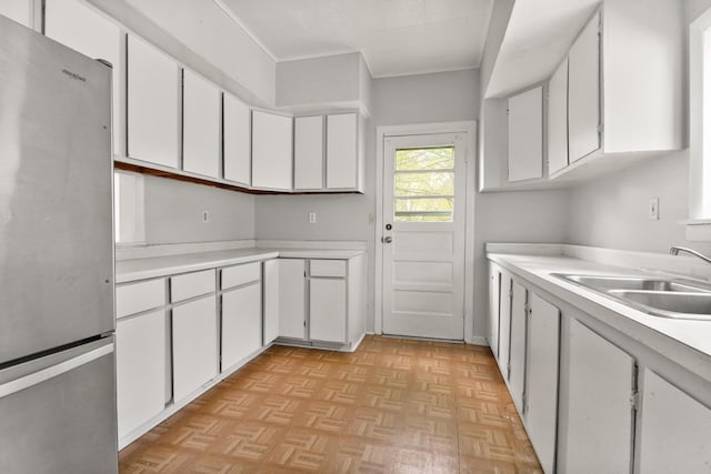 kitchen featuring freestanding refrigerator, white cabinetry, a sink, and light countertops