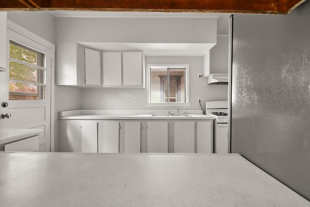 kitchen with white cabinets, a sink, light countertops, gas range gas stove, and under cabinet range hood