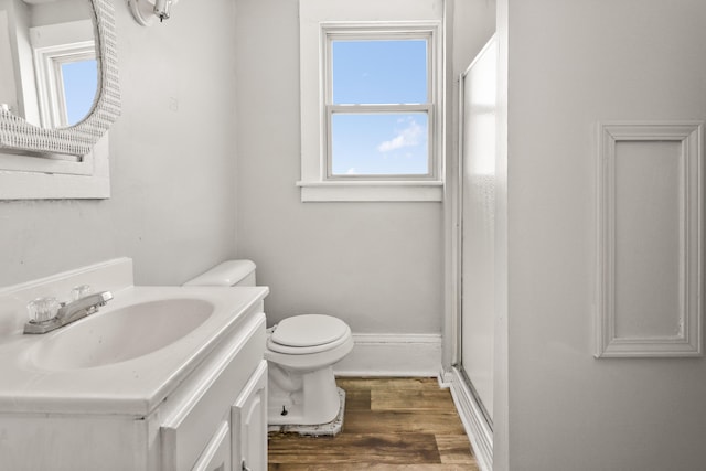 bathroom featuring vanity, toilet, baseboards, wood finished floors, and a shower with door