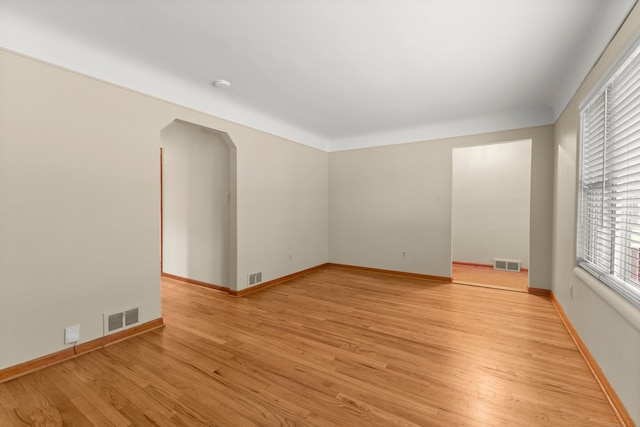 unfurnished room featuring light wood finished floors, arched walkways, baseboards, and a smoke detector