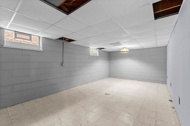 basement with plenty of natural light, a paneled ceiling, tile patterned floors, and concrete block wall