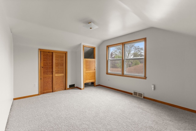 unfurnished bedroom featuring lofted ceiling, light colored carpet, baseboards, and a closet