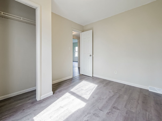unfurnished bedroom featuring baseboards, visible vents, wood finished floors, and a closet