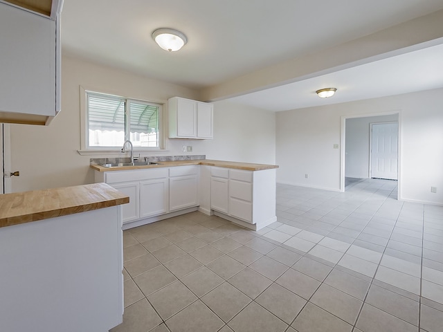 kitchen with a sink, white cabinetry, a peninsula, and light tile patterned flooring