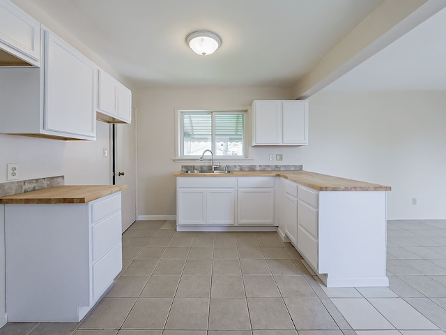 kitchen featuring butcher block countertops, a sink, a peninsula, and light tile patterned flooring