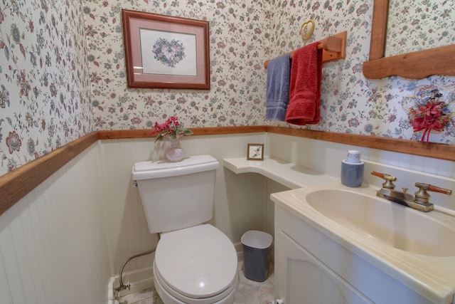bathroom featuring vanity, a wainscoted wall, toilet, and wallpapered walls