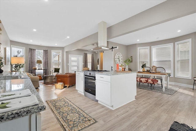 kitchen featuring island range hood, stainless steel gas range oven, light wood finished floors, open floor plan, and white cabinetry