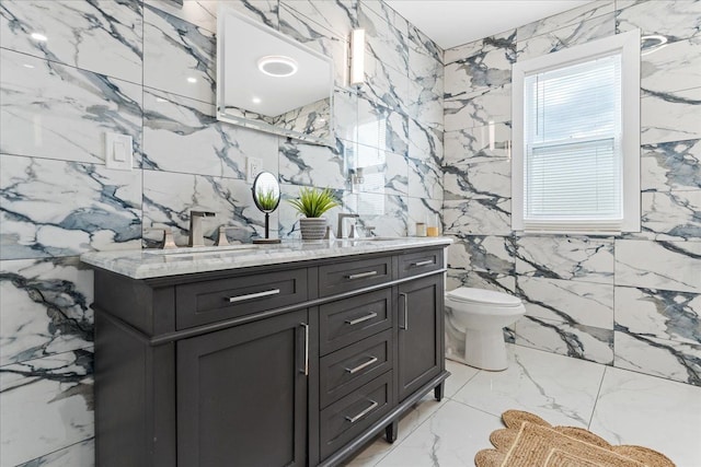 full bath with a sink, double vanity, toilet, marble finish floor, and tile walls