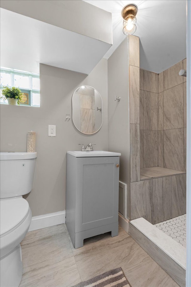 bathroom with vanity, baseboards, a tile shower, and toilet