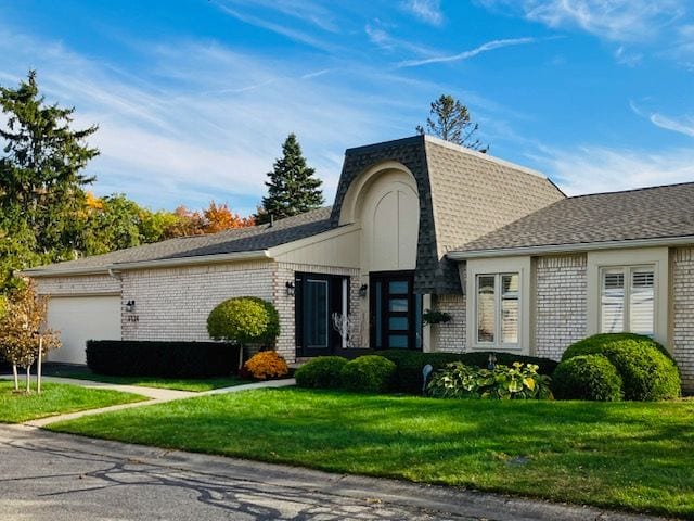 view of property with brick siding, an attached garage, and a front yard
