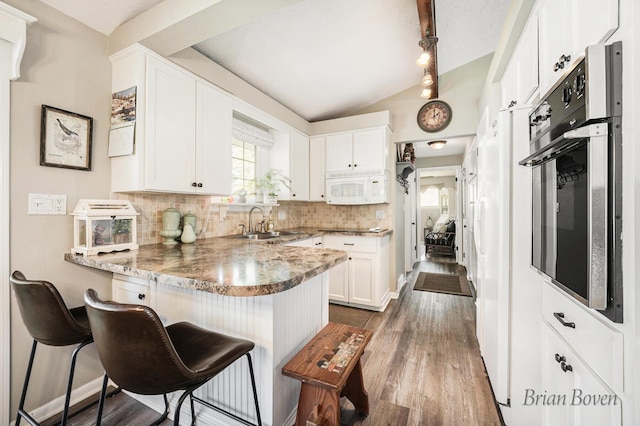 kitchen with decorative backsplash, a sink, white cabinets, white microwave, and a peninsula