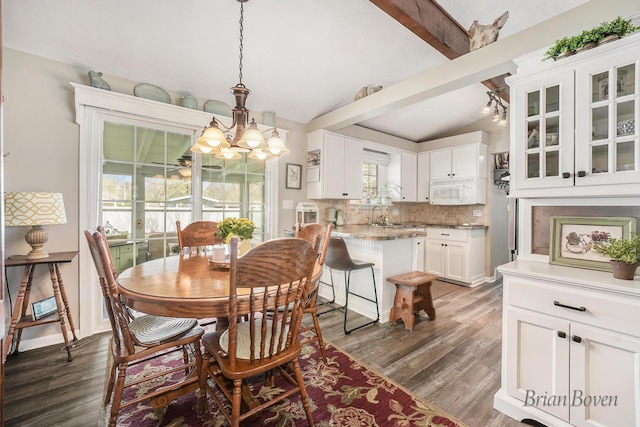 dining room featuring vaulted ceiling with beams, plenty of natural light, wood finished floors, and a chandelier