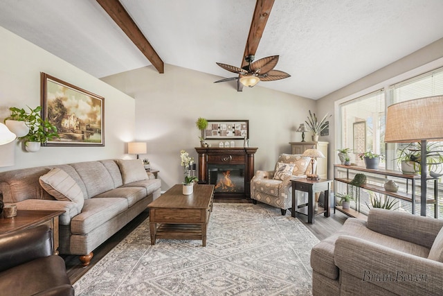 living room with a lit fireplace, ceiling fan, lofted ceiling with beams, and light wood-style floors