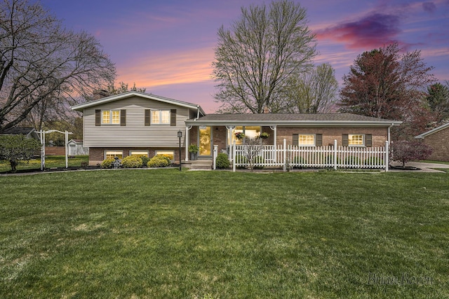 split level home featuring a yard, brick siding, fence, and covered porch