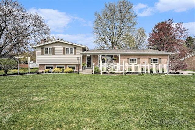 tri-level home with brick siding, fence, a chimney, and a front lawn
