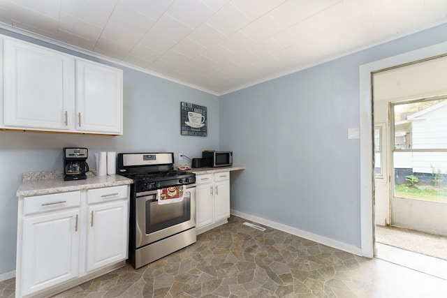 kitchen with crown molding, appliances with stainless steel finishes, light countertops, white cabinetry, and stone finish flooring