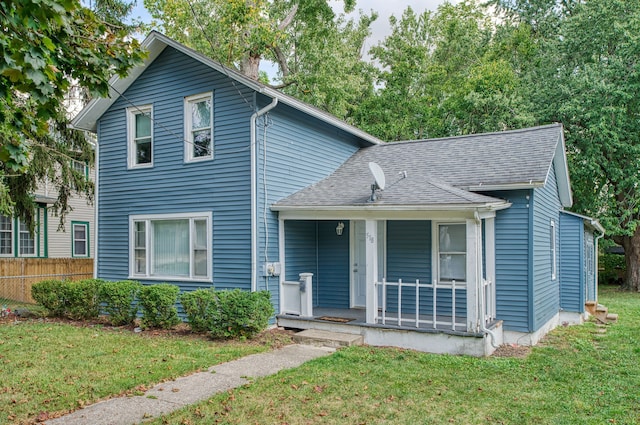traditional-style home featuring covered porch, fence, a shingled roof, and a front yard