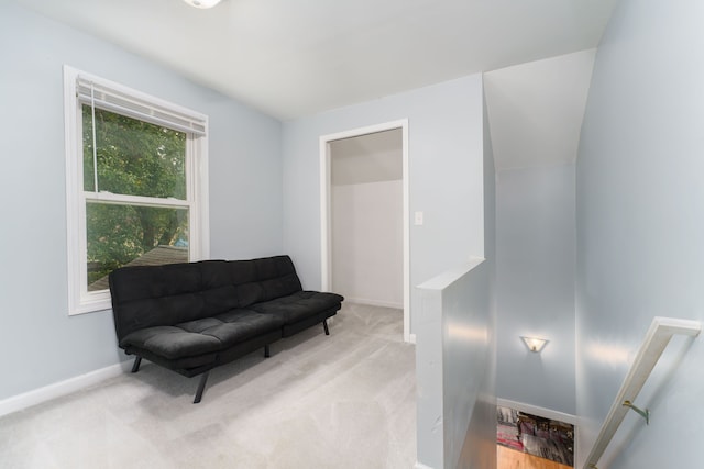 living area featuring baseboards, light carpet, and an upstairs landing