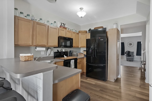 kitchen featuring black appliances, a sink, a peninsula, and light wood-type flooring