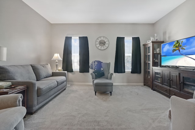 living area featuring healthy amount of natural light, baseboards, and light carpet