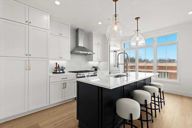 kitchen with a sink, light countertops, light wood-type flooring, and wall chimney exhaust hood