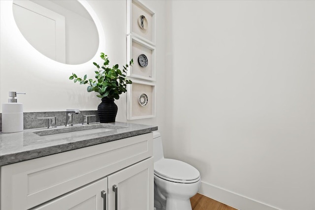 bathroom with vanity, baseboards, wood finished floors, and toilet