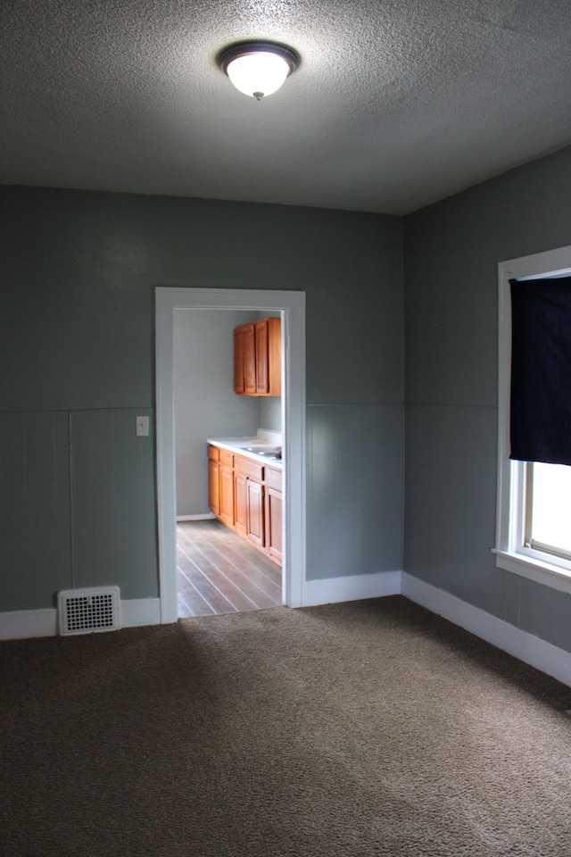 unfurnished room featuring baseboards, visible vents, a textured ceiling, and light colored carpet