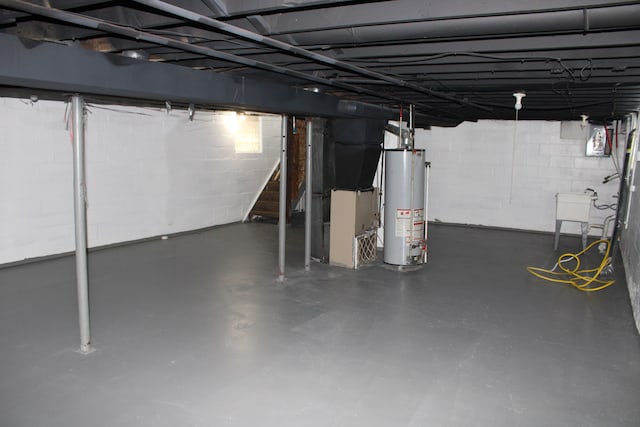 unfinished basement featuring concrete block wall, a sink, gas water heater, and stairway